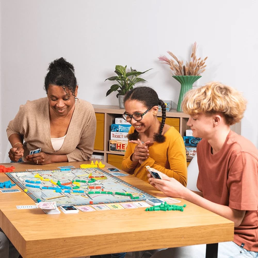 Drie mensen spelen samen Ticket to Ride aan de keukentafel